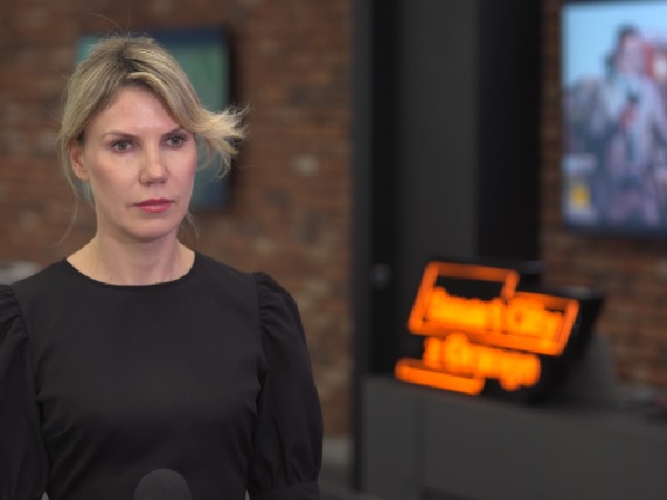 Portret blondynki w czarnej sukience, o poważnym wyrazie twarzy.