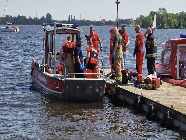 Ratownicy na łodzi i na nabrzeżu udzielają pomocy ludziom po wypadku na wodzie.