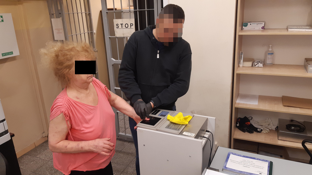 Policjant pobierający odciski palców od starszej kobiety na posterunku
