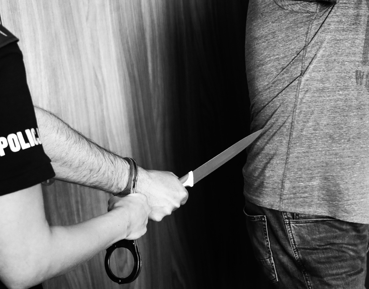 Policjant aresztujący podejrzanego z nożem i kajdankami
