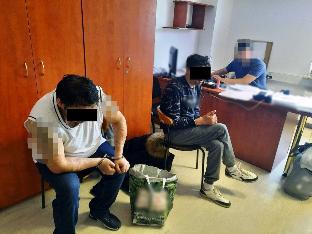 Trzech skutych kajdankami mężczyzn siedzi w pokoju przesłuchań na komisariacie policji.