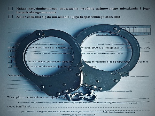 Kajdanki na dokumencie polskiego zakazu zbliżania się. Widoczne są komunikaty „Nakaz natychmiastowego opuszczenia” i „Zakaz przygotowania się”.