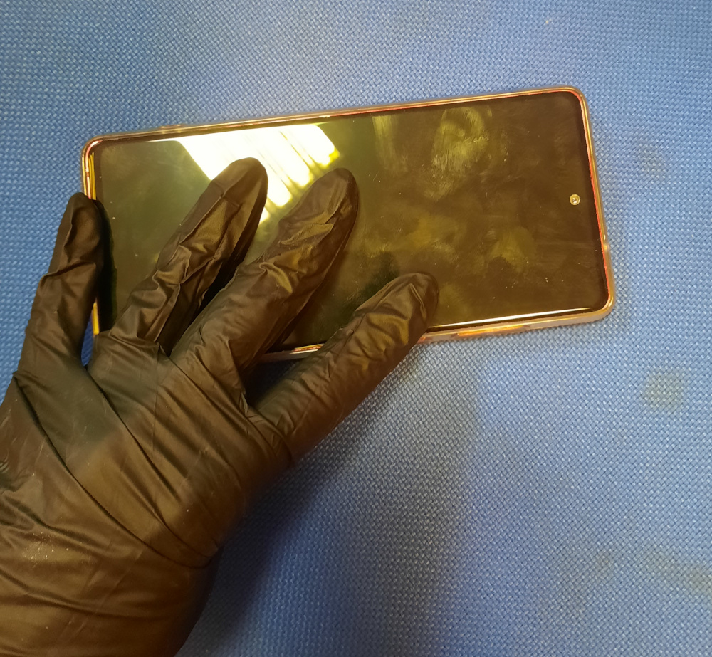 Dłoń w rękawiczce sprawdzająca ekran smartfona pod kątem uszkodzeń.