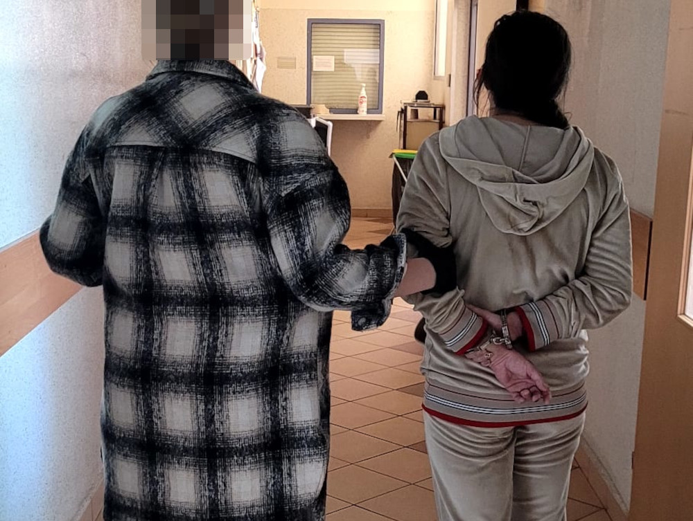 Widok z tyłu dwóch skutych kajdankami osób eskortowanych korytarzem.