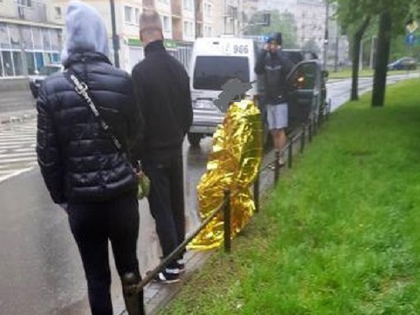 Ludzie stoją w pobliżu wypadku samochodowego, jedna osoba jest owinięta złotym kocem ratunkowym.