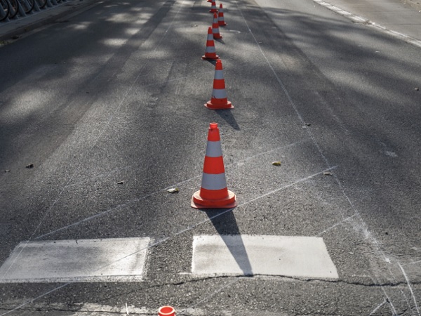 Pachołki drogowe ustawione wzdłuż ulicy wraz z oznaczeniami przejść dla pieszych.