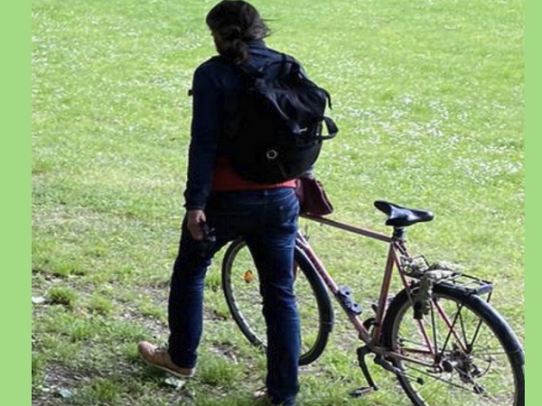Osoba z plecakiem przechodząca obok roweru na trawiastej ścieżce