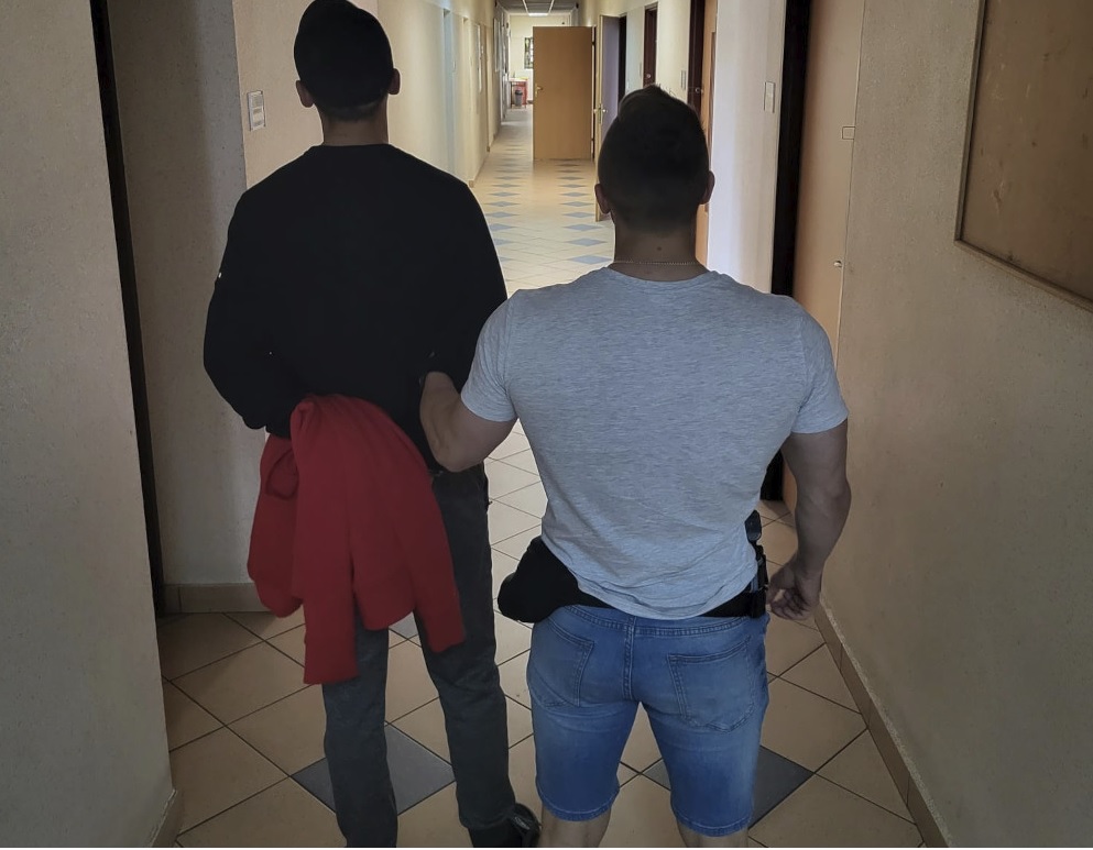 Dwóch mężczyzn idących korytarzem, jeden w areszcie.