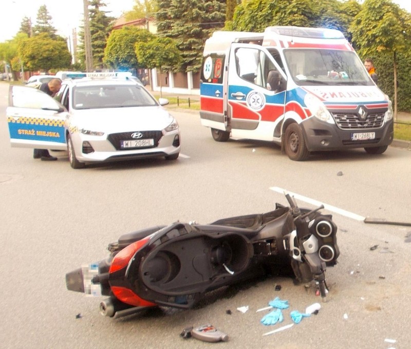 Uszkodzony skuter po wypadku drogowym, na miejscu pojawiła się policja i karetka pogotowia.