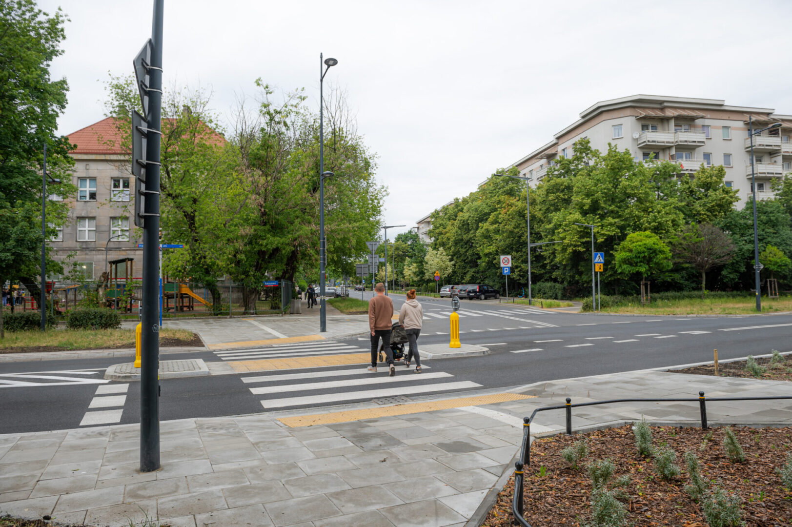 Para z wózkiem dziecięcym przechodzi przez przejście dla pieszych na skrzyżowaniu w mieście