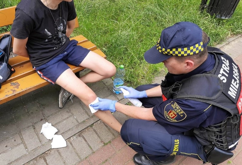 Ratownik udzielający pierwszej pomocy przy urazie kolana na ławce w parku