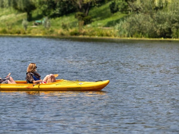 Dwie osoby płyną kajakiem po spokojnym jeziorze, ciesząc się słonecznym dniem.