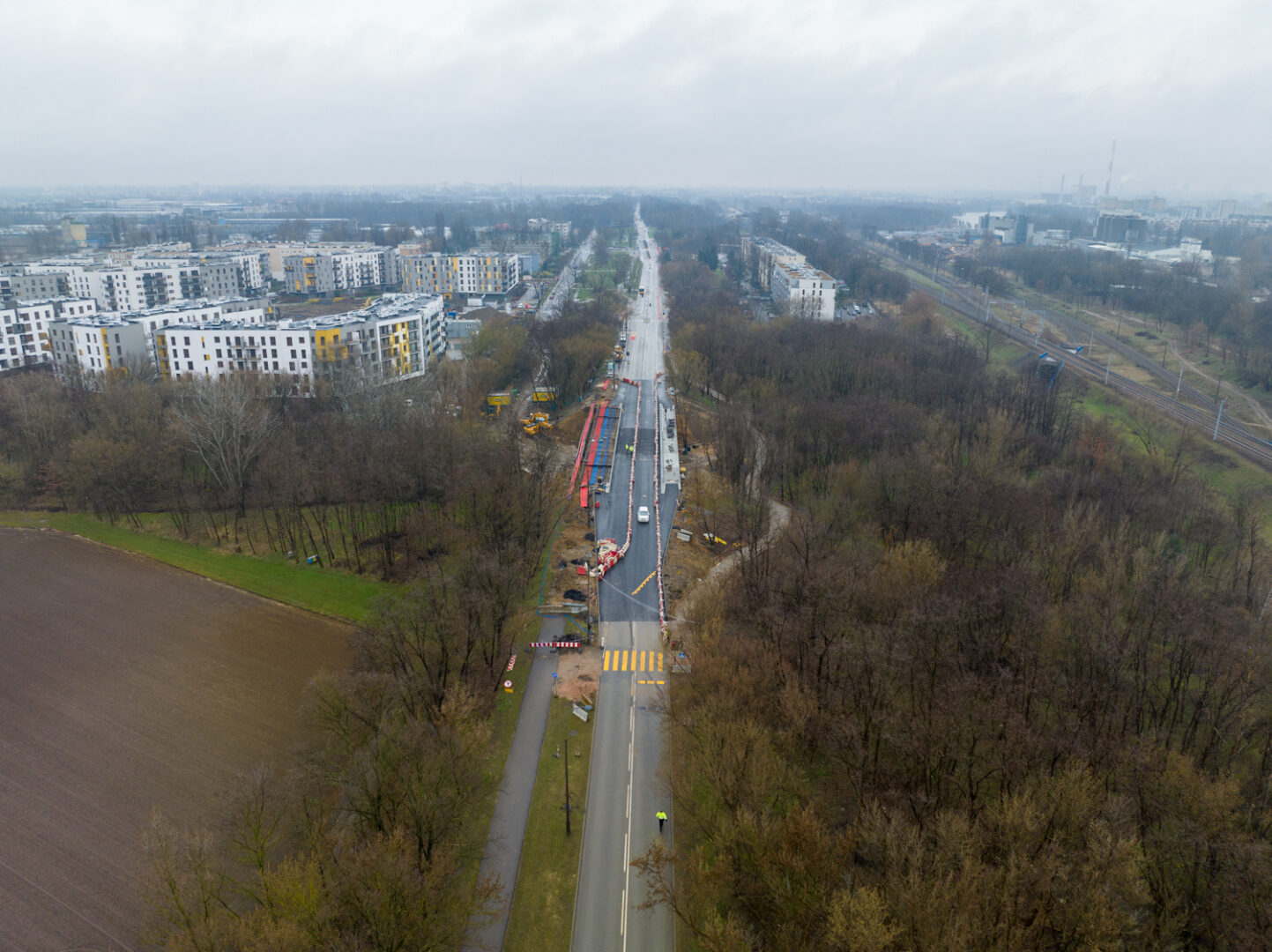 Widok z lotu ptaka na budowę drogi, nowe budynki mieszkalne i otaczający park.
