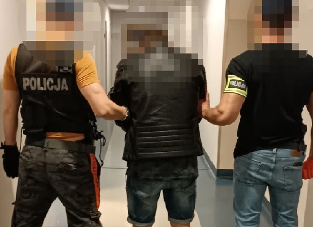 Policjanci zatrzymują podejrzanego na korytarzu. Na kamizelce jednego z funkcjonariuszy widać napis „POLICJA”.