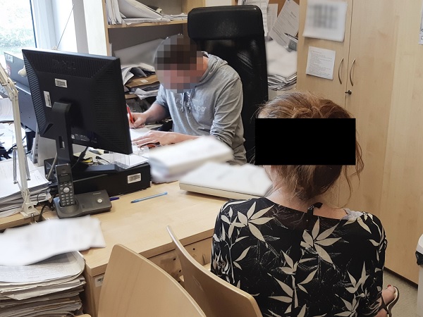 Dwie osoby pracujące przy biurkach, przeglądające dokumenty.