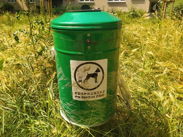 Zielony kosz na psie odchody z napisem „Posprzątaj po swoim psie”.