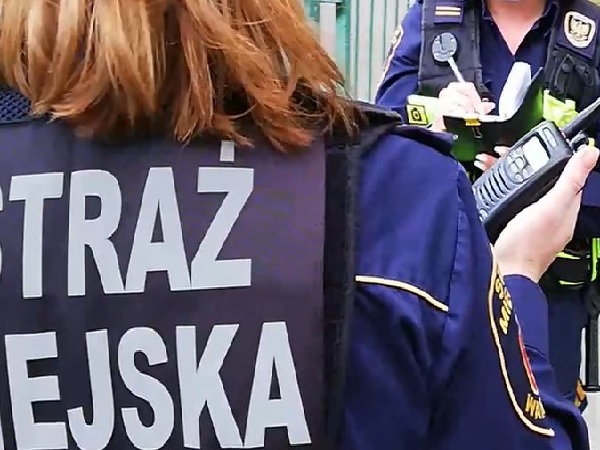 Funkcjonariusz Straży Miejskiej korzystający z radia, piszący notatki