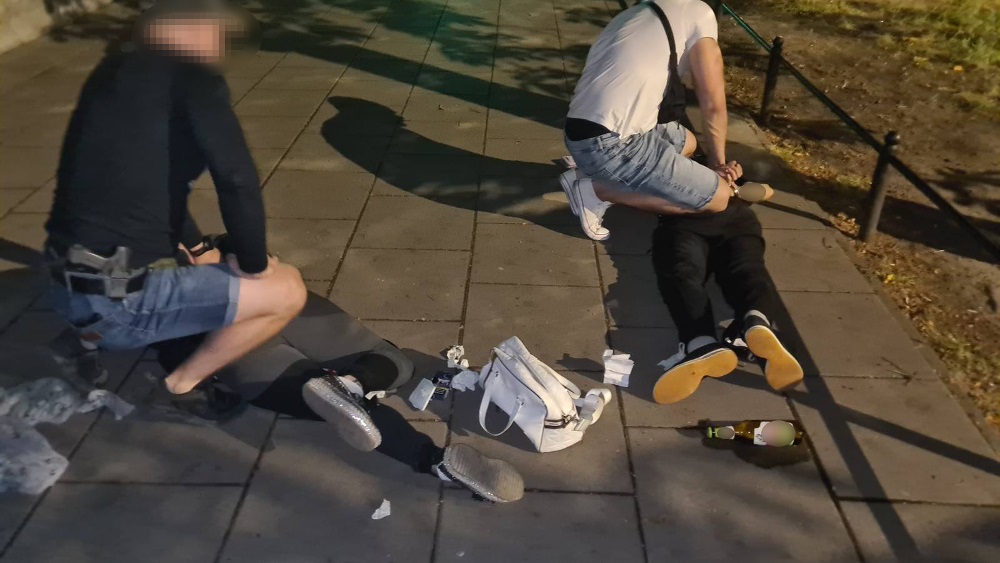 Policjanci aresztują podejrzanego na ziemi w nocy. Dowody są rozrzucone w pobliżu.