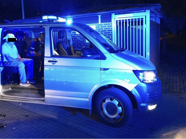 Policyjny furgon nocą z dwoma zatrzymanymi podejrzanymi w środku.