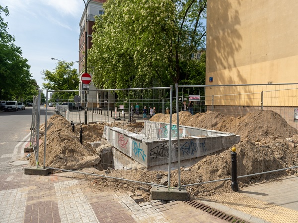 Plac budowy z wykopanym wykopem, stosami ziemi i tymczasowym ogrodzeniem.