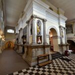Bogato zdobione wnętrze kościoła ze statuami, ołtarzem i szachownicową podłogą.