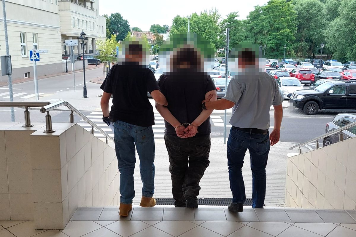 Dwóch policjantów eskortuje skutego podejrzanego po schodach.