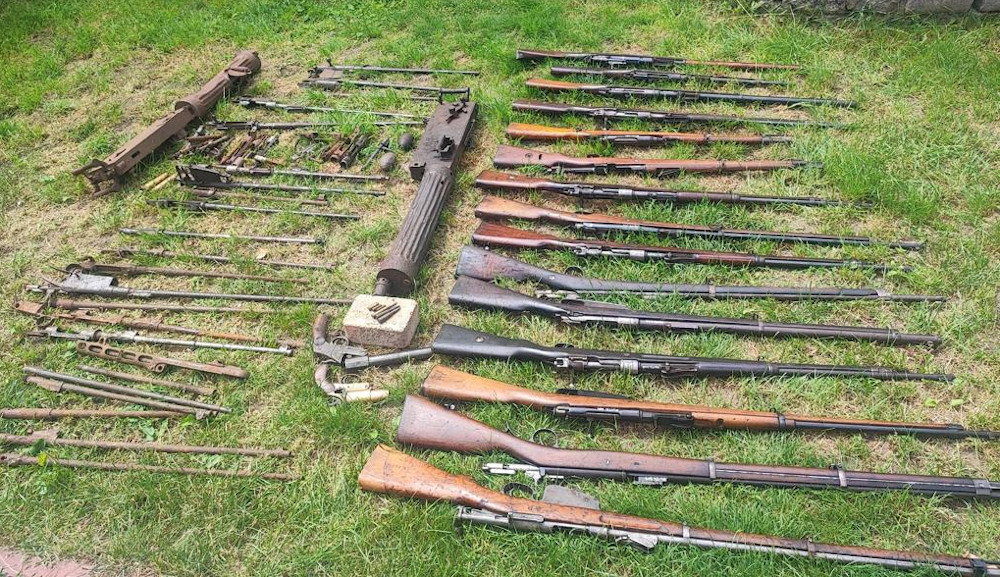Zdemontowany karabin maszynowy z czasów I wojny światowej oraz liczne karabiny wystawione na trawie.