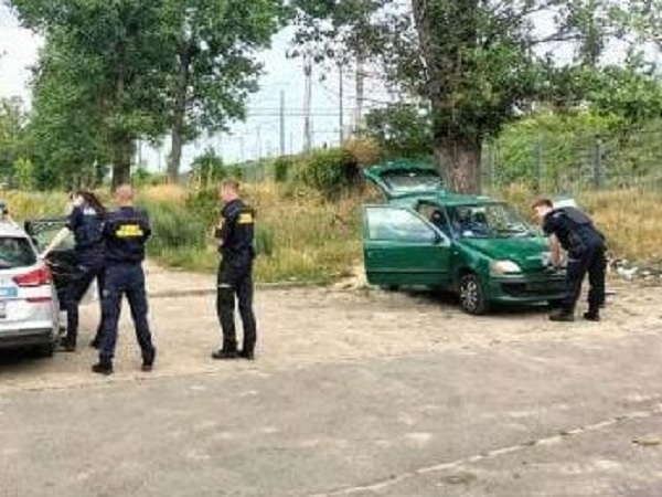 Policjanci badający zielony samochód Fiat na miejscu zbrodni.