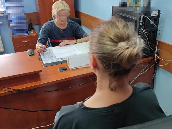 Dwie kobiety przy biurku, jedna wypełnia dokumenty.