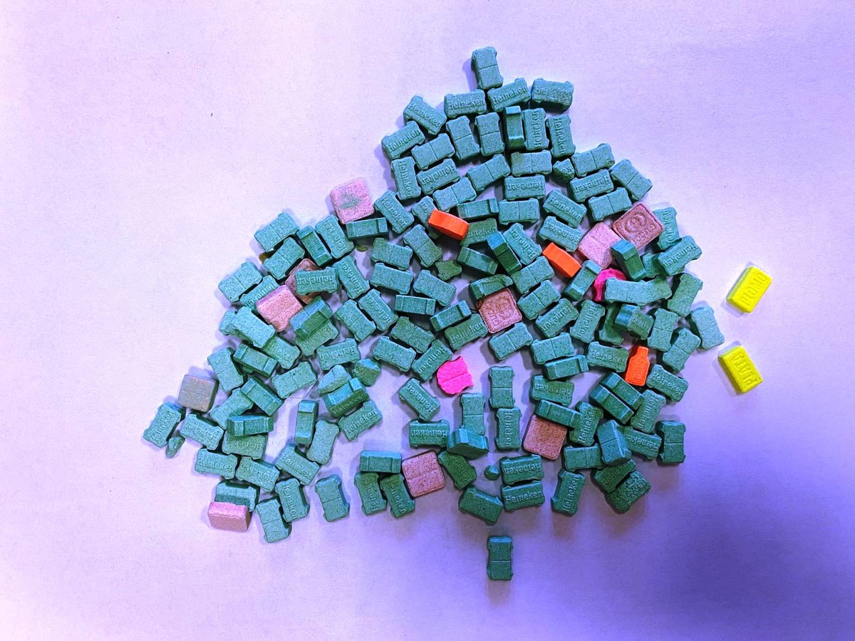 Stos kolorowych tabletek MDMA, niektóre pomarańczowe, różowe i żółte.