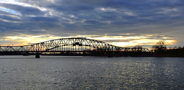Stalowy most kratownicowy nad rzeką o zachodzie słońca