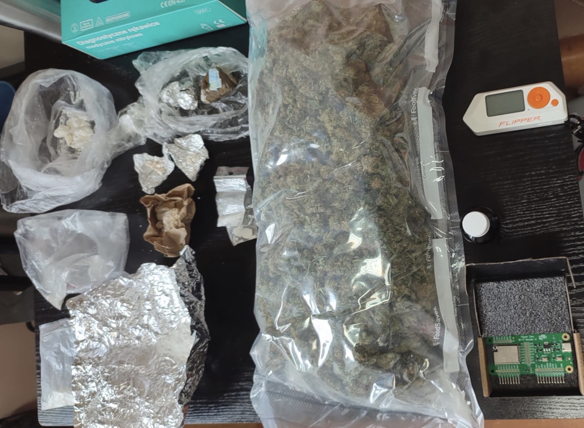 Na ciemnej powierzchni wyeksponowano różne narkotyki i przyrządy do ich zażywania, w tym marihuanę, wagi i materiały opakowaniowe.