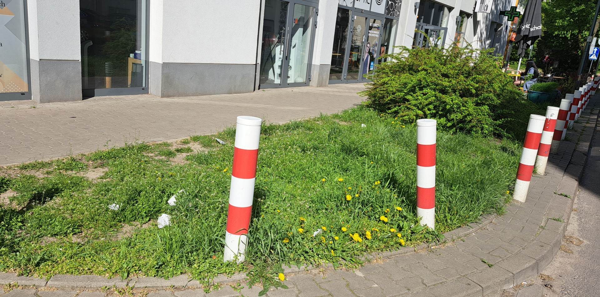 Czerwono-białe słupki wyznaczają trawiasty obszar obok budynku.