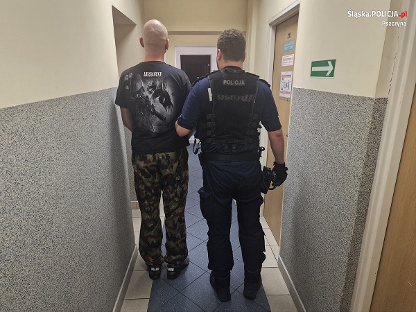 Policjant eskortujący podejrzanego korytarzem.