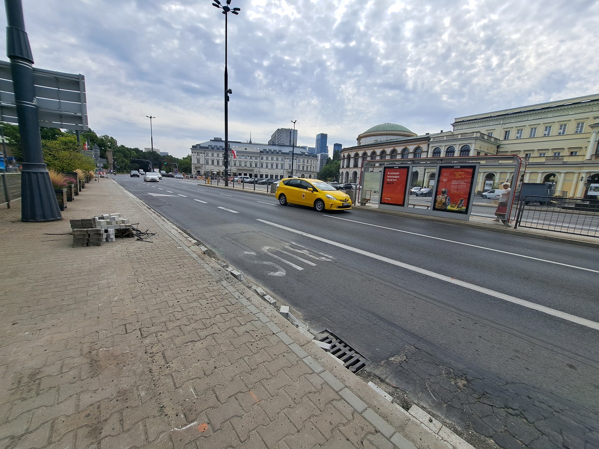 Scena uliczna Warszawy z żółtą taksówką, przystankiem autobusowym i budową ulicy