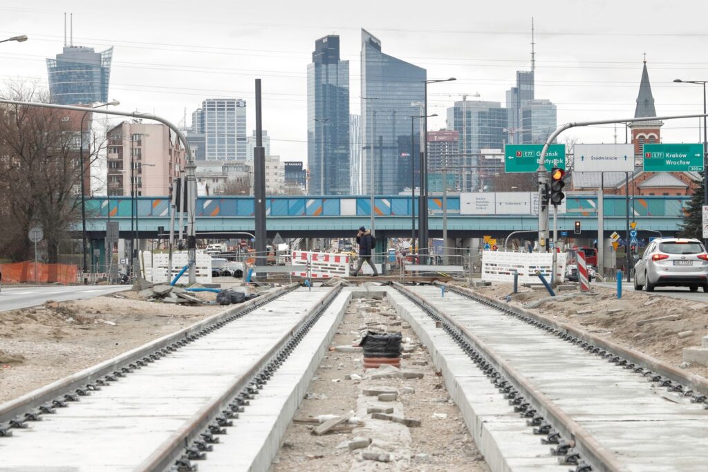 Tory tramwajowe w budowie w Warszawie, na tle nowoczesnej panoramy miasta.