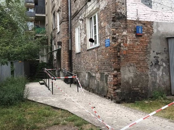 Zniszczony budynek z cegły z rampą i taśmą ostrzegawczą. Widoczny numer 8.