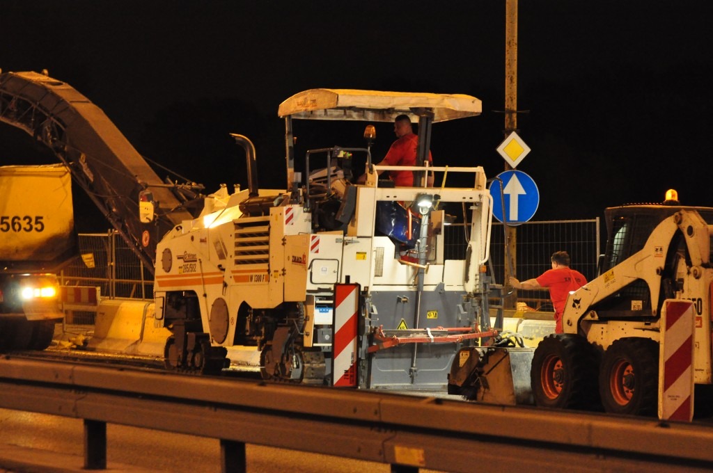 Ekipa drogowa w nocy używa frezarki i ładowarki kołowej