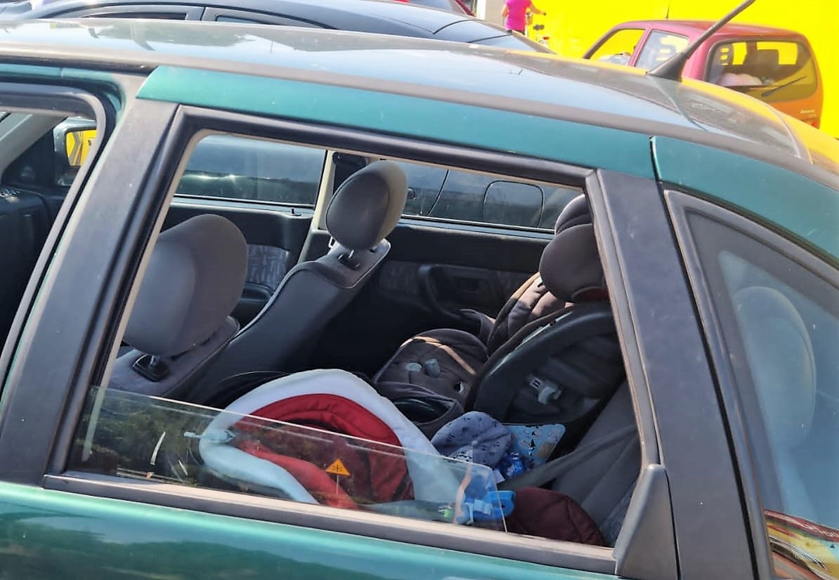 Wnętrze zielonego samochodu z dwoma fotelikami dziecięcymi i akcesoriami dla niemowląt.