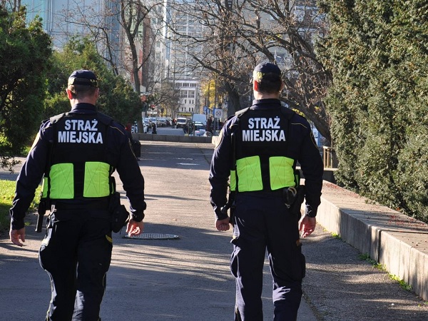 Dwóch polskich Strażników Miejskich patroluje ulicę miasta.