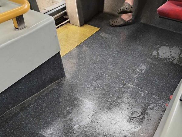 Brudna podłoga autobusu z pasażerami w Crocsach i żółtą poręczą