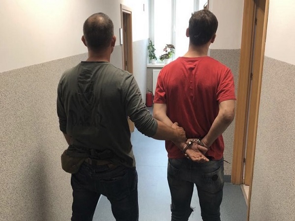 Policjant eskortujący skutego kajdankami podejrzanego korytarzem.