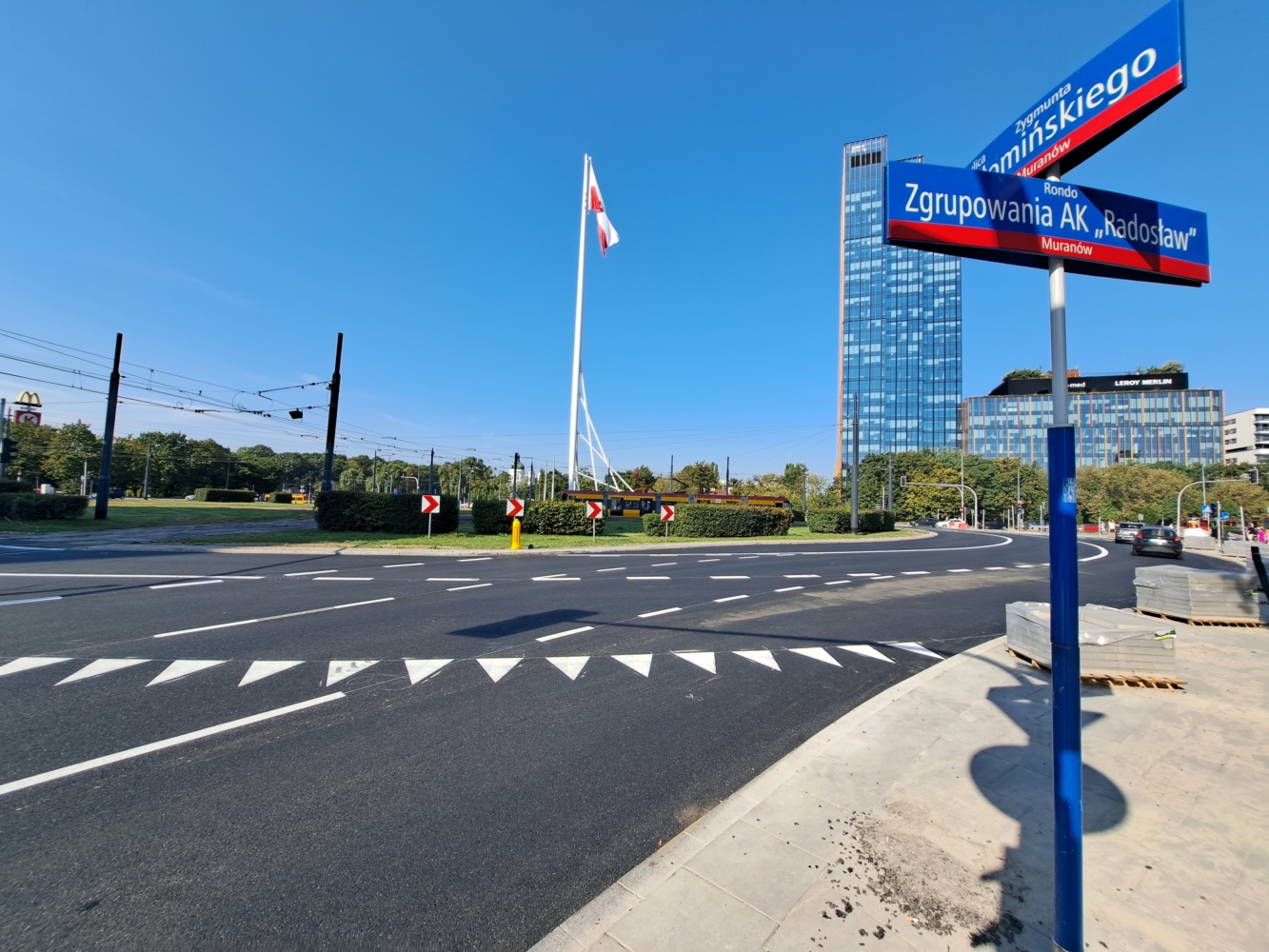 Widok na Warszawską ulicę przy rondzie Zgrupowania AK "Radosław", z polską flagą i nowoczesnymi budynkami.