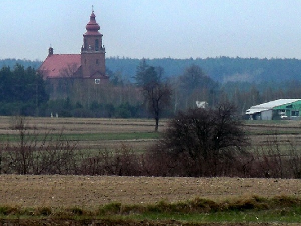 Daleki widok na kościół z czerwonym dachem na tle wiejskiego krajobrazu.