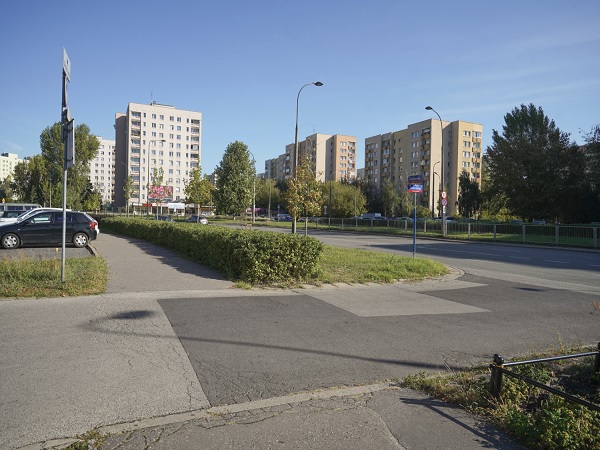 Scena uliczna z budynkami mieszkalnymi, zielenią i zaparkowanymi samochodami.