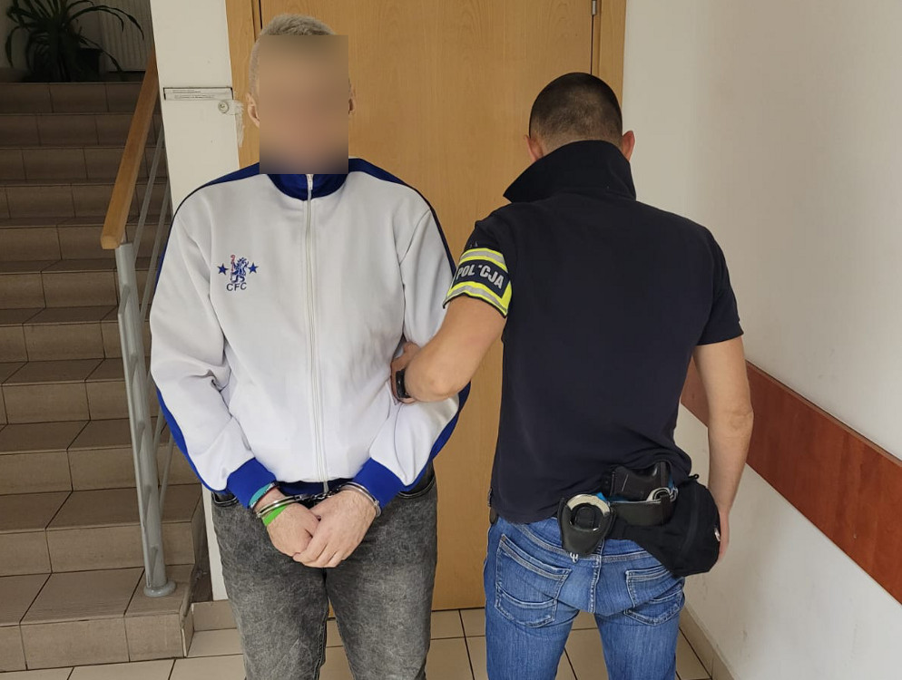 Policjant aresztujący podejrzanego w kajdankach na korytarzu budynku.