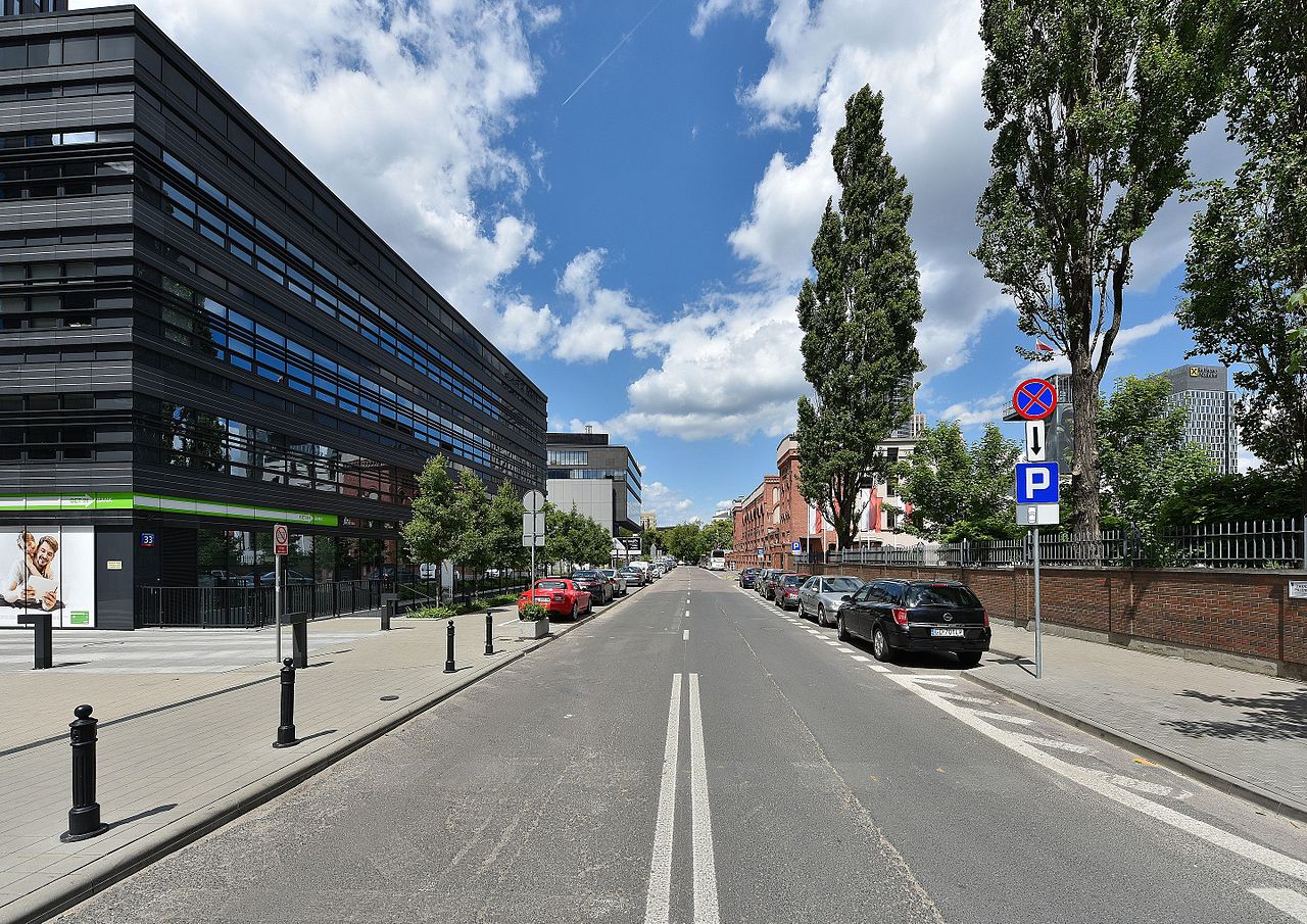 Nowoczesny widok ulicy miejskiej z zaparkowanymi samochodami, ukazujący mieszankę współczesnej i starszej architektury.