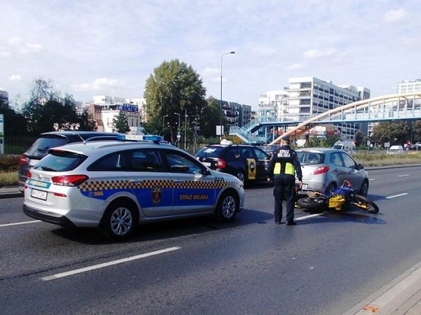Scena wypadku motocyklowego z udziałem radiowozu i policjanta.