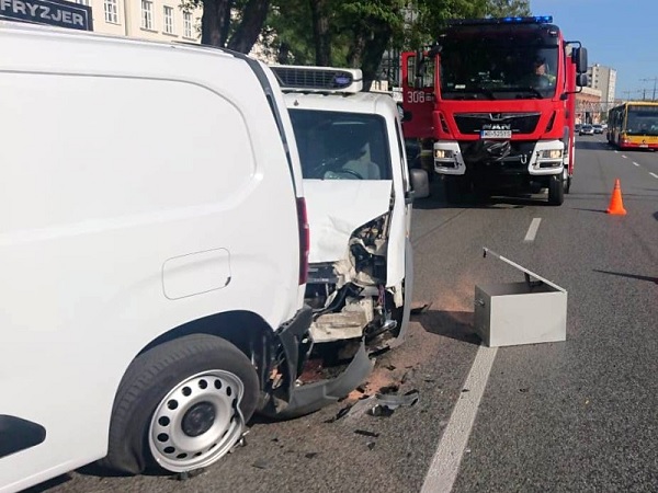 Uszkodzony biały van po wypadku samochodowym, w tle wóz strażacki.
