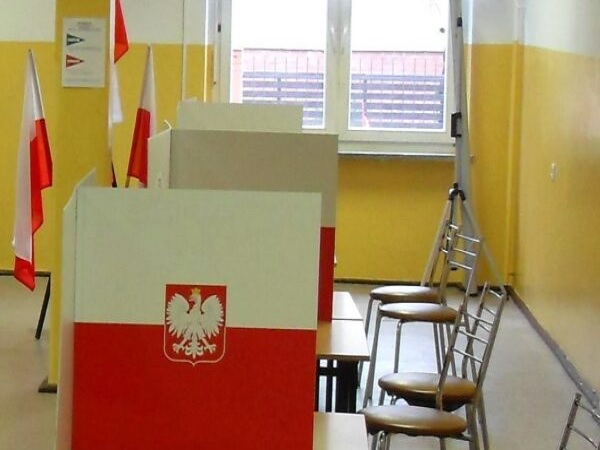 Polski lokal wyborczy z kabinami do głosowania i polskimi flagami.